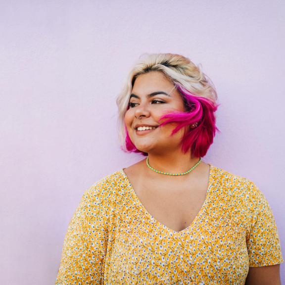 Young white woman with blond and pink hair looking to her side and smiling on lavender background