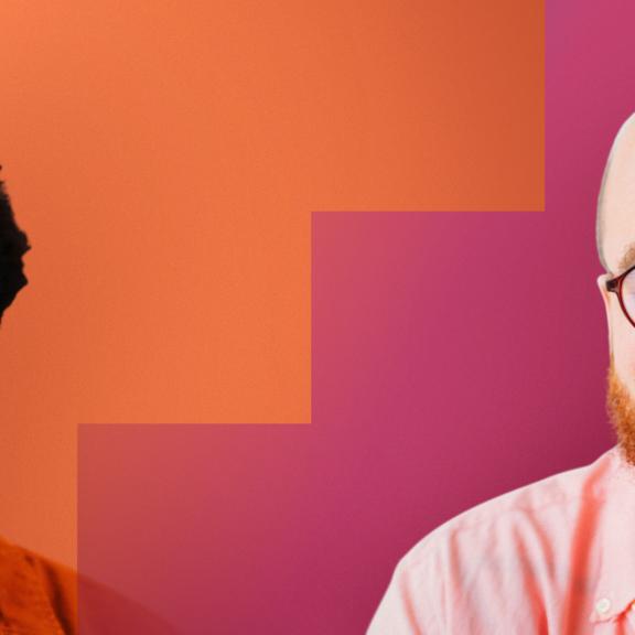 A black young man and a young balding white man with glasses smiling with a colourful background